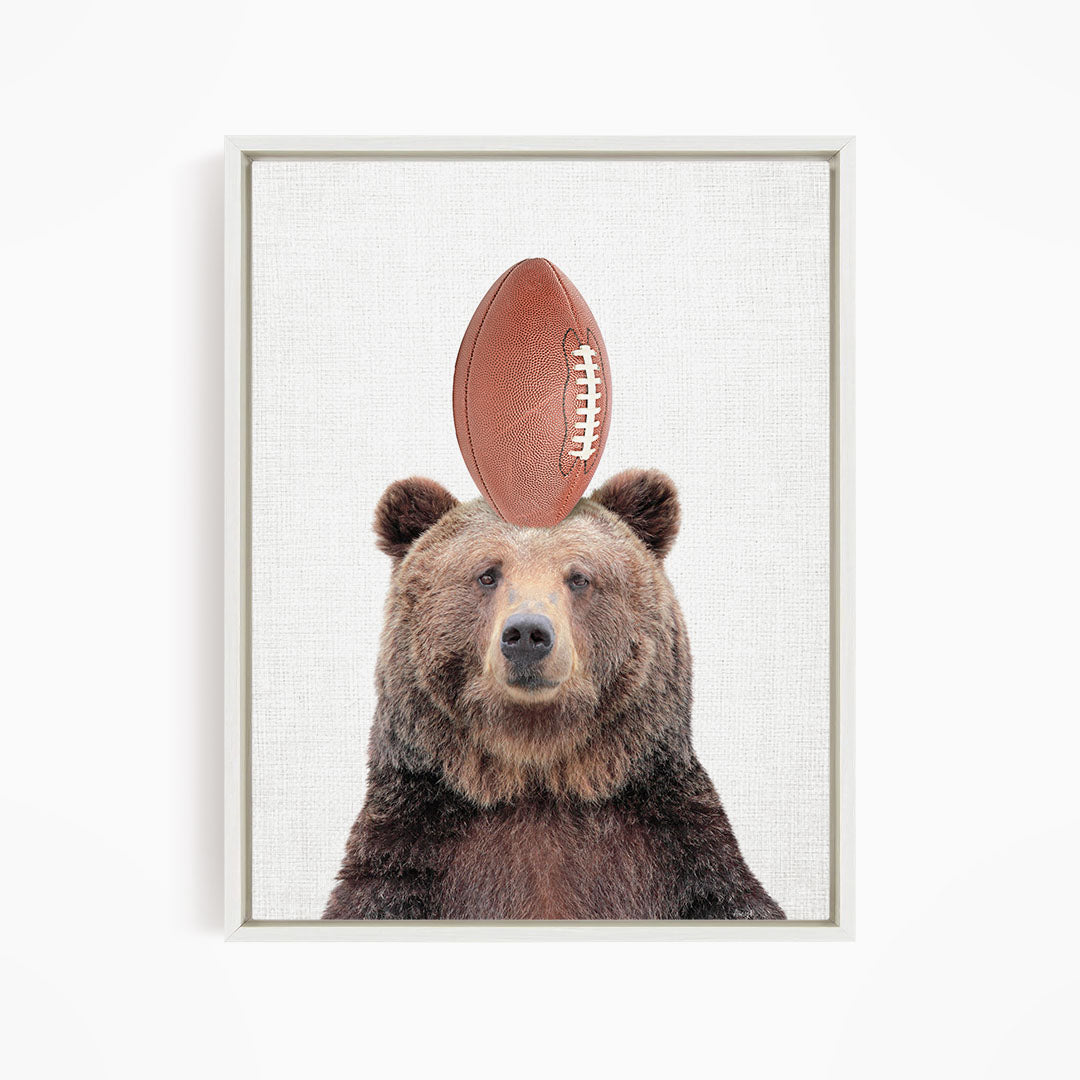 A brown bear standing on a football, with the football positioned on top of its head.
