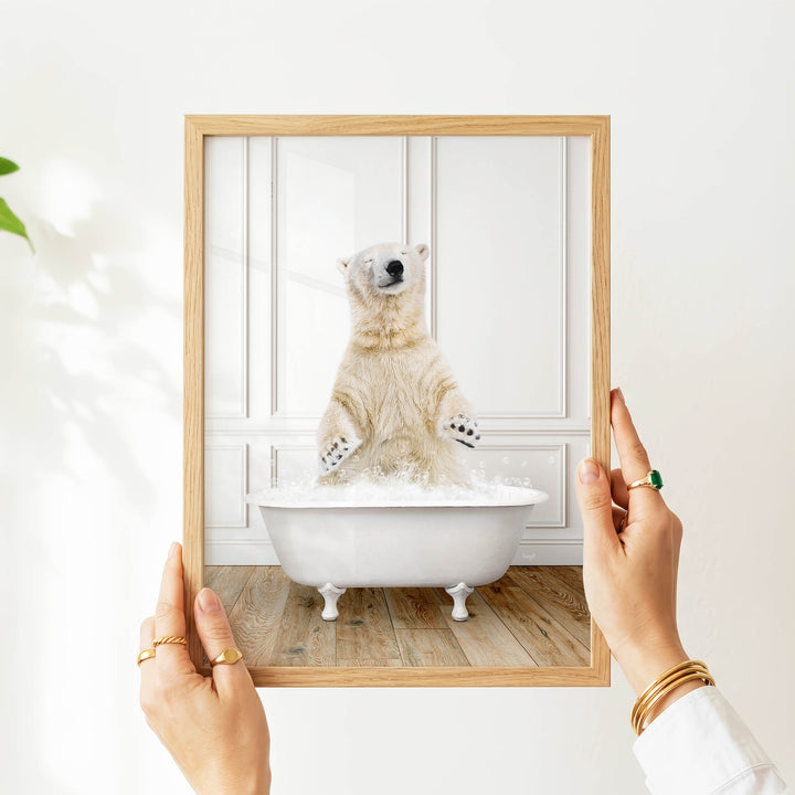 A person's hands are holding a picture frame containing a photograph of a polar bear sitting in a bathtub filled with water.