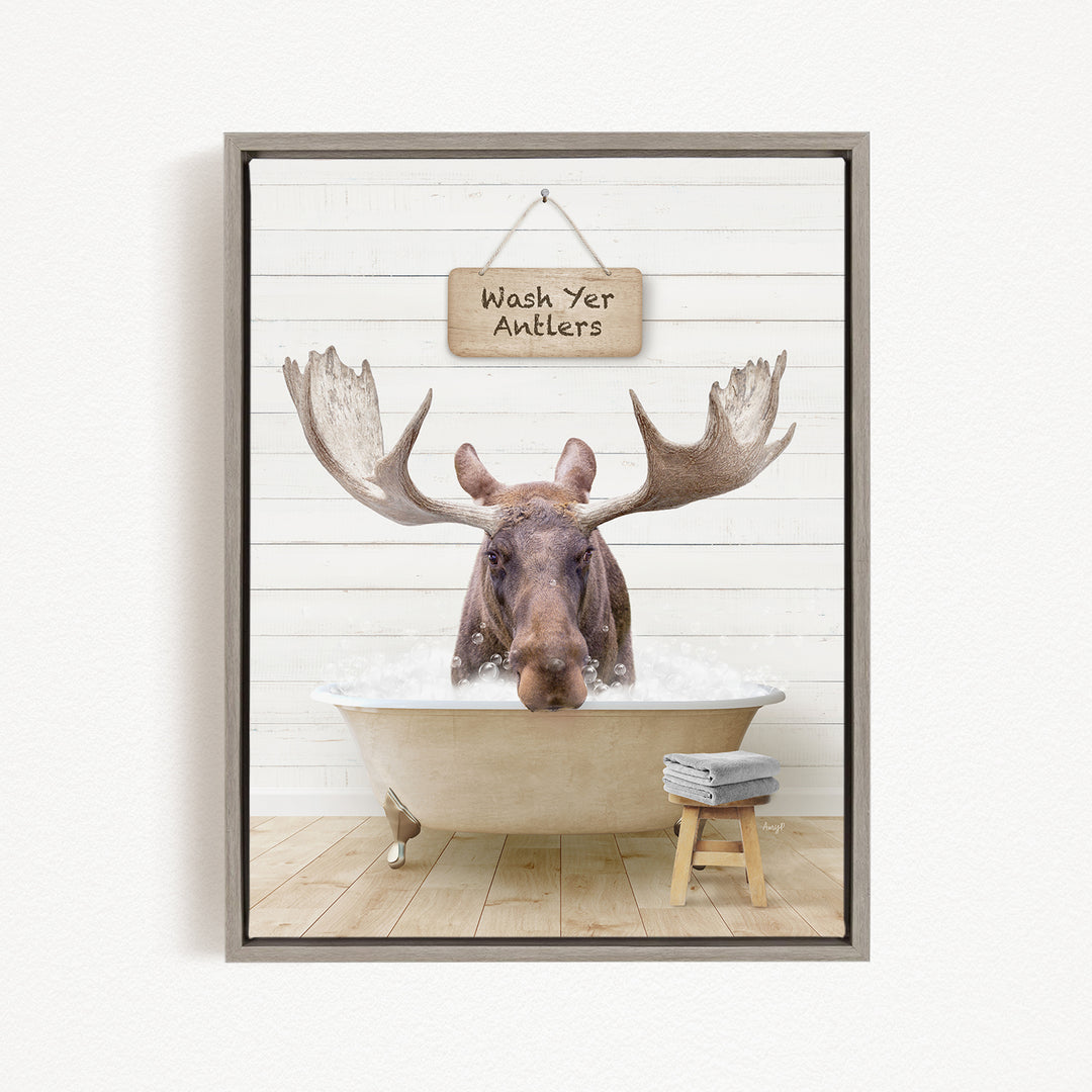 A moose is sitting in a bathtub filled with water, with a sign above it that says "Wash Yer Antlers".