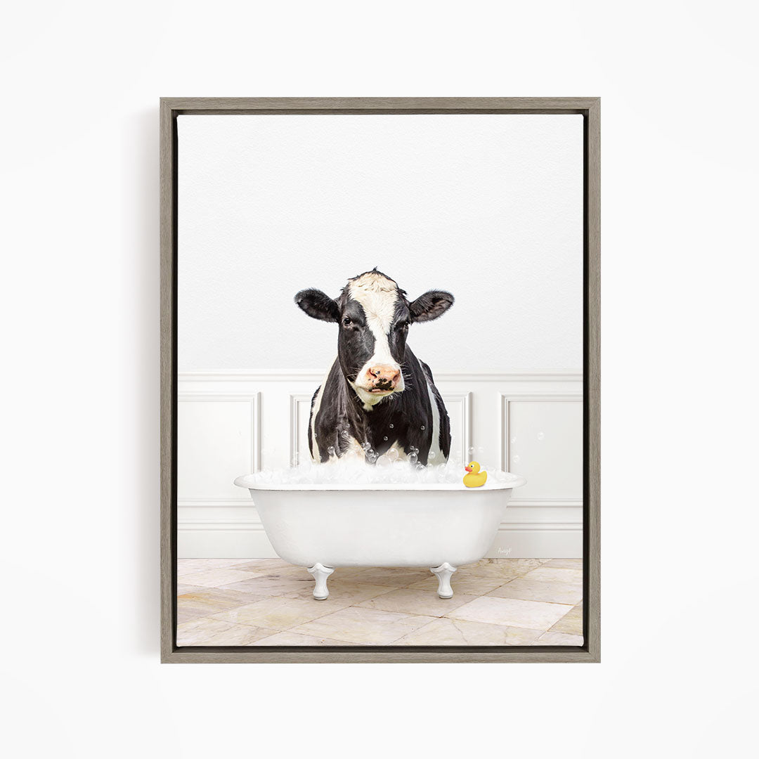 A black and white cow is standing in a white bathtub filled with water, with a rubber duck floating in the water.