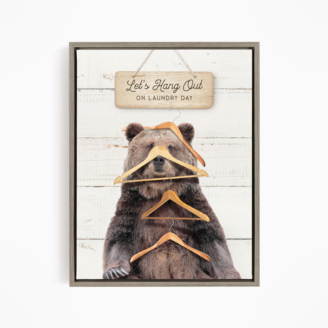 A framed image of a bear sitting on a wooden surface, with a sign above it that says "Let's Hang Out on Laundry Day".