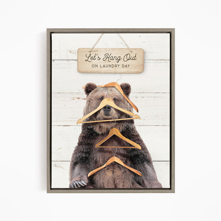 A framed image of a bear sitting on a wooden surface, with a sign above it that says "Let's Hang Out on Laundry Day".