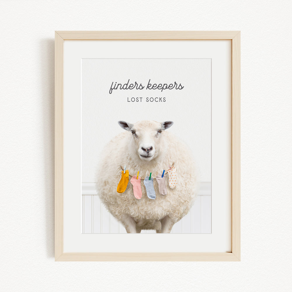A framed image of a sheep wearing colorful socks, with the text "finders keepers" and "lost socks" above the sheep.