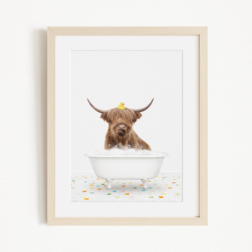 A brown cow with long horns is sitting in a white bathtub filled with bubbles, with a yellow rubber duck perched on its head.
