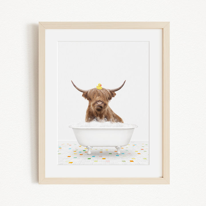 A brown cow with long horns is sitting in a white bathtub filled with bubbles, with a yellow rubber duck perched on its head.