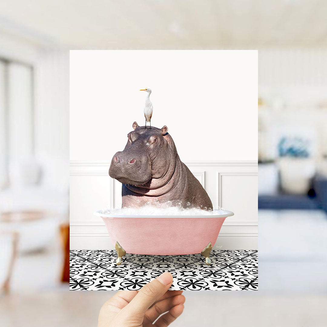 A hand holds up a framed image of a hippopotamus sitting in a pink bathtub, with a seagull perched on its head.