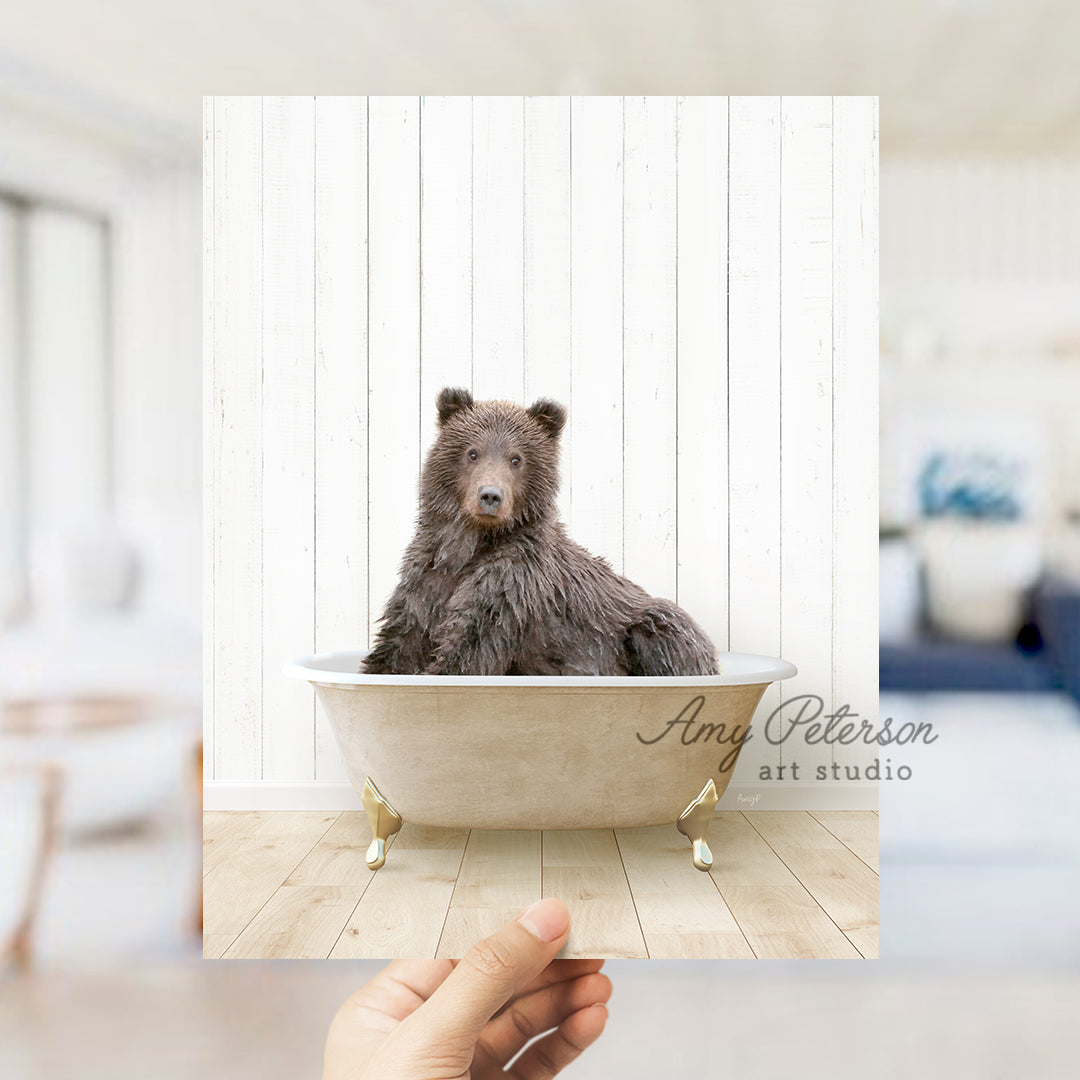 a hand holding a photo of a bear in a bathtub