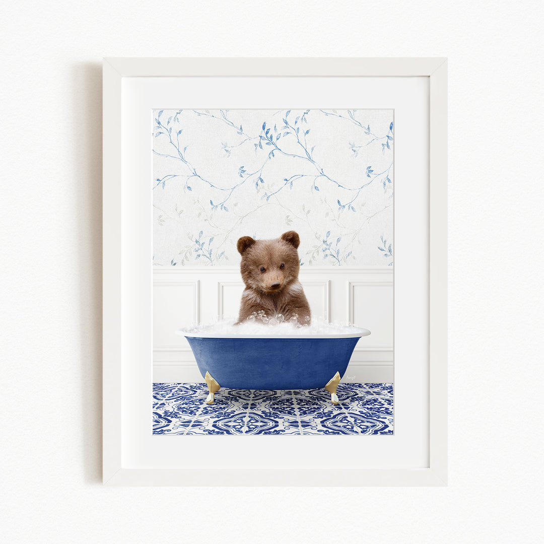 A cute brown bear sitting in a blue bathtub filled with bubbles, surrounded by a blue and white patterned rug.