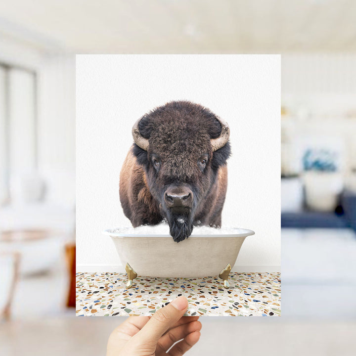 A close-up of a bison's head in a bathtub, with a hand holding the photo up to the camera.
