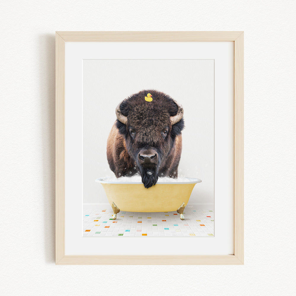 A buffalo with a yellow rubber duck perched on its head is sitting in a yellow bathtub, surrounded by a colorful tiled floor.