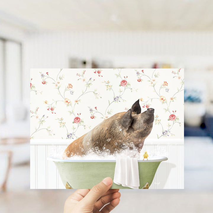 A hand holds up a collage of two images: one showing a pig sitting in a bathtub filled with bubbles, and the other showing a duck sitting in the same bathtub.