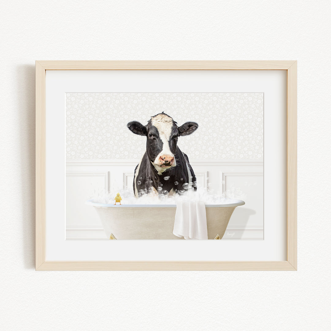 A black and white cow is sitting in a white bathtub filled with bubbles, creating a whimsical and playful scene.