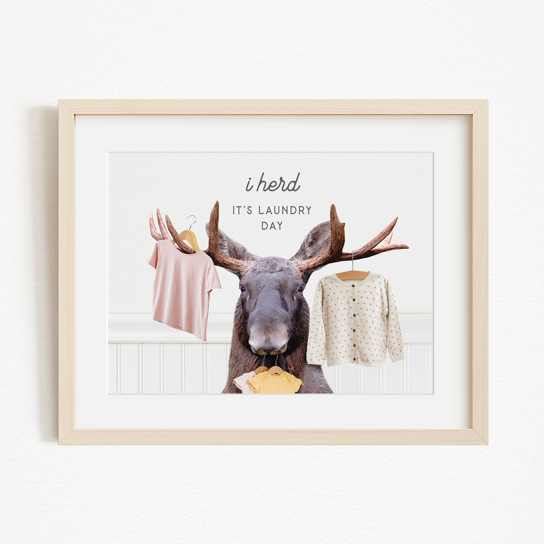 A framed image depicting a moose with antlers holding clothes, accompanied by the text "It's laundry day"
