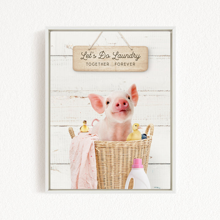 A cute pig sitting in a wicker basket filled with various toys, including a yellow duck and a pink blanket, with a wooden sign above that says "Let's Do Laundry Together Forever".