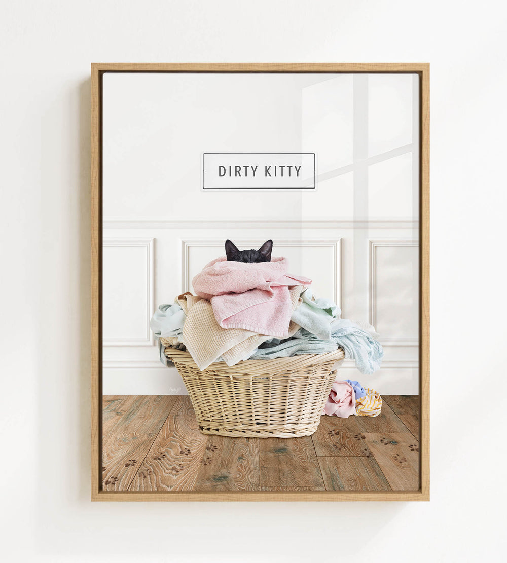 A framed image of a cat sitting in a basket filled with clothes, with the text "Dirty Kitty" displayed above the basket.