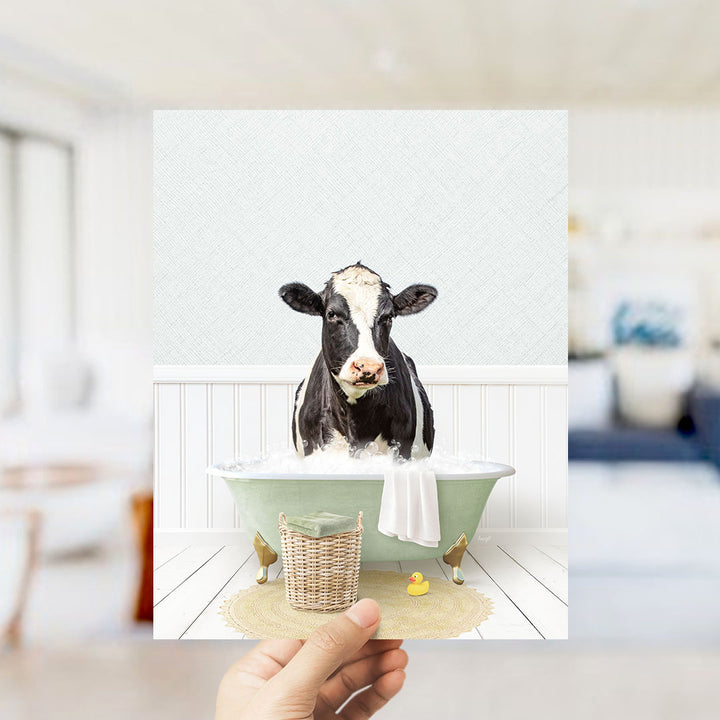 A black and white cow is sitting in a green bathtub filled with bubbles, with a yellow rubber duck nearby.