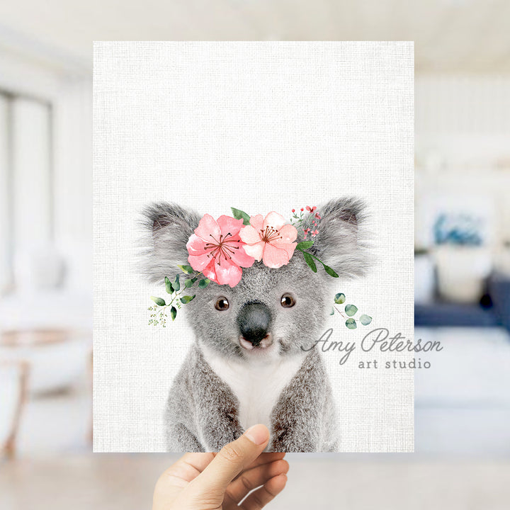 a hand holding up a card with a koala bear wearing a flower crown