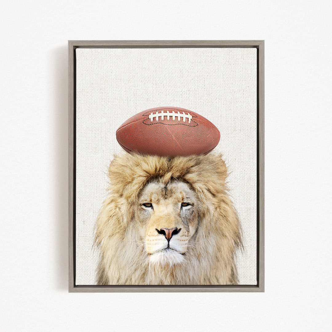 A lion with a football on its head, looking directly at the camera.