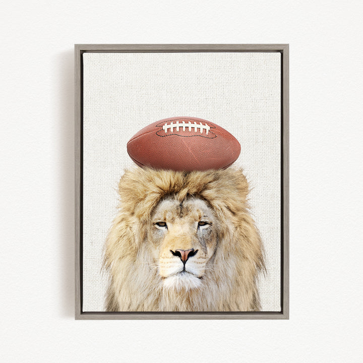 A lion with a football on its head, looking directly at the camera.