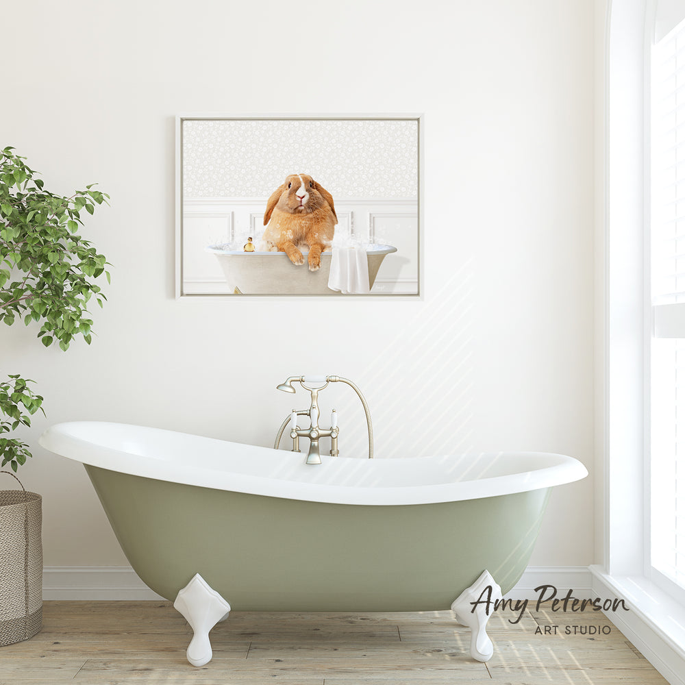 A framed image of a dog sitting in a bathtub is displayed on the wall above a green clawfoot bathtub in a bright, white-walled bathroom.