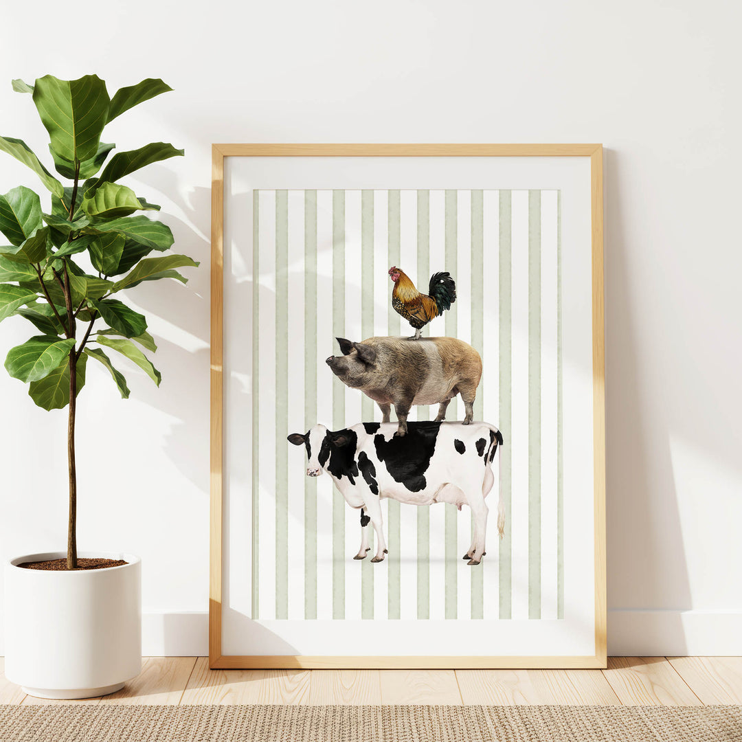A framed print of a pig, cow, and rooster standing on top of each other, with a potted plant to the left.