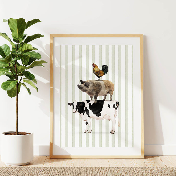 A framed print of a pig, cow, and rooster standing on top of each other, with a potted plant to the left.