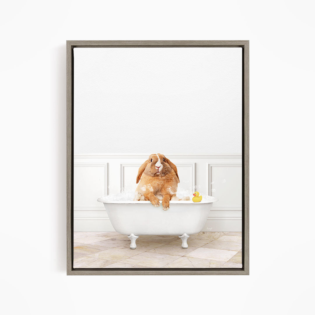 A brown rabbit sitting in a white bathtub filled with bubbles, with a rubber duck floating nearby.