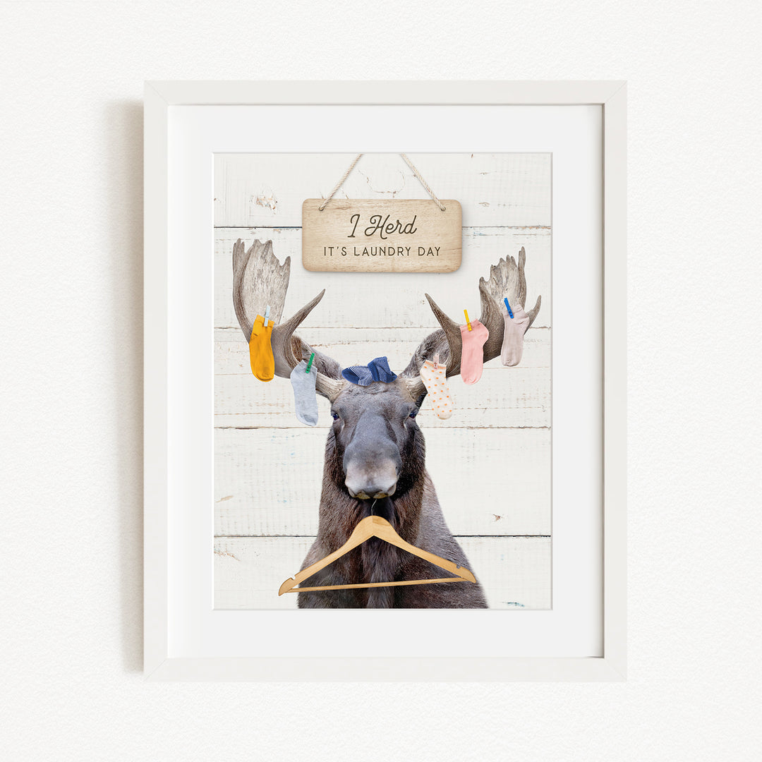 A framed image depicting a moose with a sign above it that says "I herd, it's laundry day".
