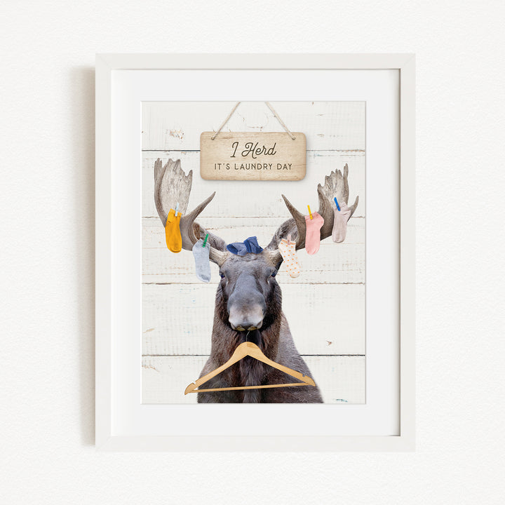 A framed image depicting a moose with a sign above it that says "I herd, it's laundry day".