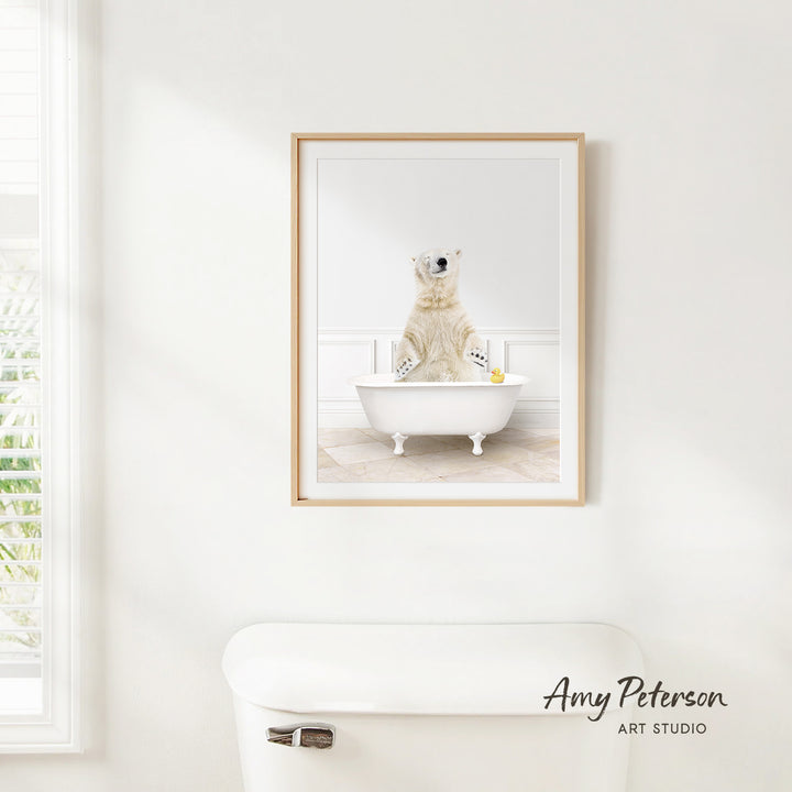 A framed image of a polar bear sitting in a bathtub, with a window and toilet visible in the background.