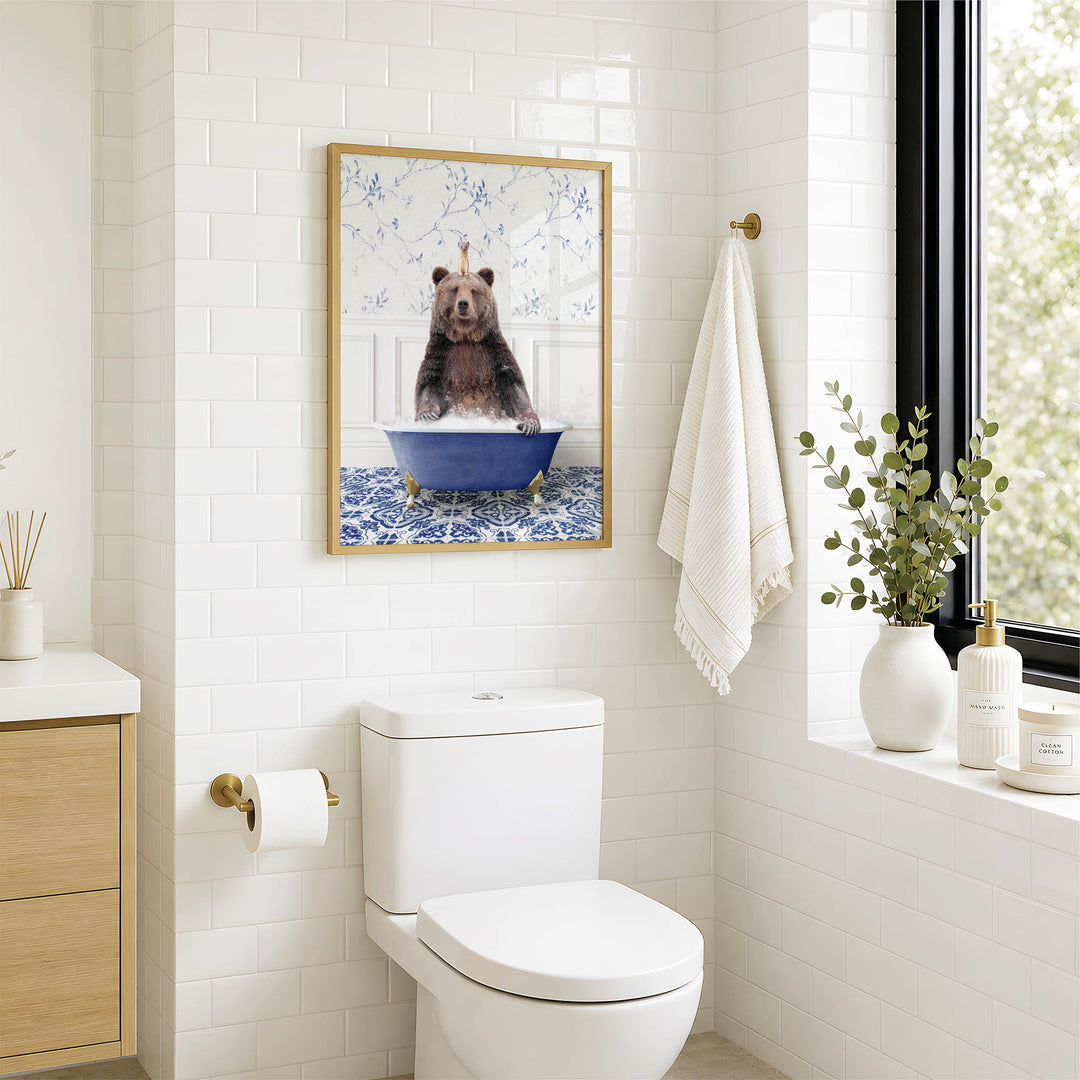 A bathroom with a white toilet, a framed image of a bear sitting in a blue bathtub, and a window with greenery outside.