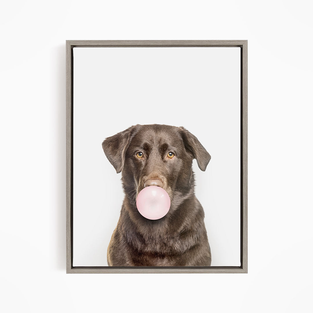 A brown dog is blowing a bubble with a pink bubble gum bubble.