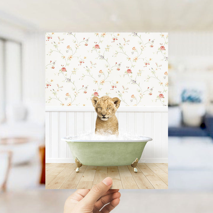 A young lion cub sitting in a green bathtub filled with water, surrounded by a floral wallpaper.
