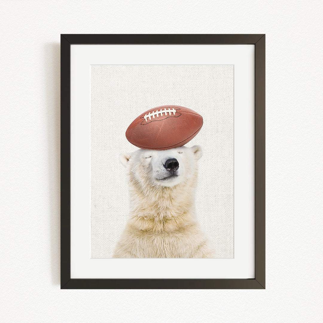 A polar bear is sitting on a football, with its eyes closed, in a framed picture.