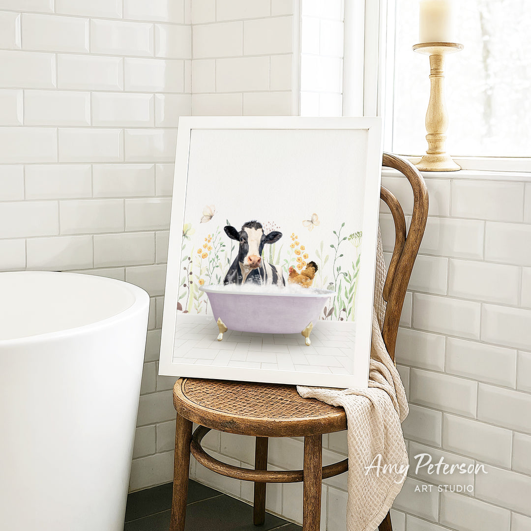 A framed painting depicting a cow and a chicken relaxing in a bathtub, surrounded by flowers, is displayed on a wooden chair in a bathroom setting.