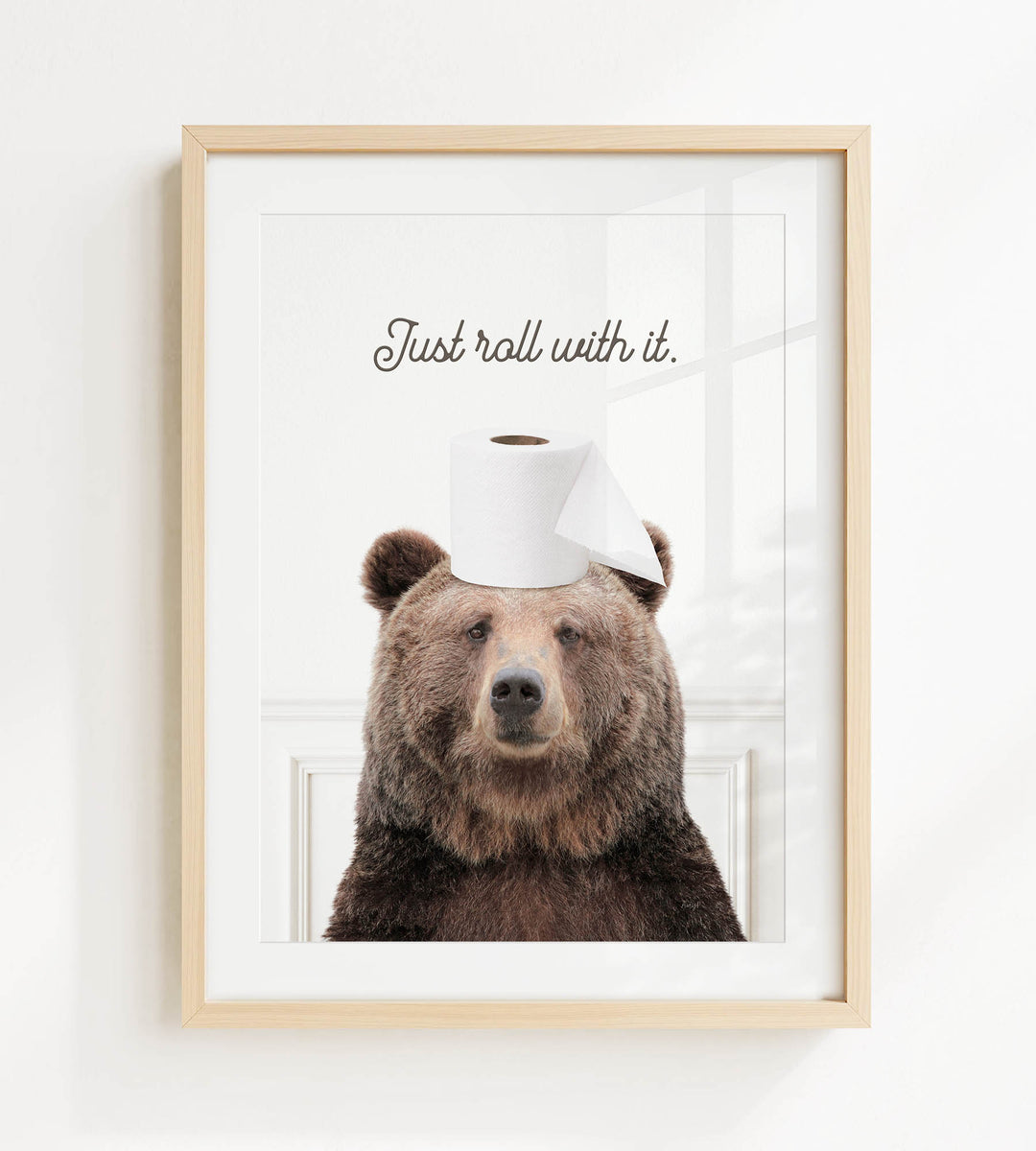 A framed image of a brown bear wearing a roll of toilet paper on its head, with the text "Just roll with it."