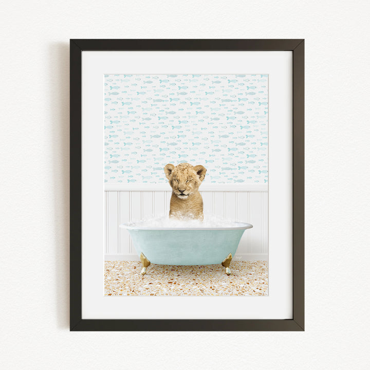A young lion cub sitting in a blue bathtub filled with water, surrounded by a patterned wall.
