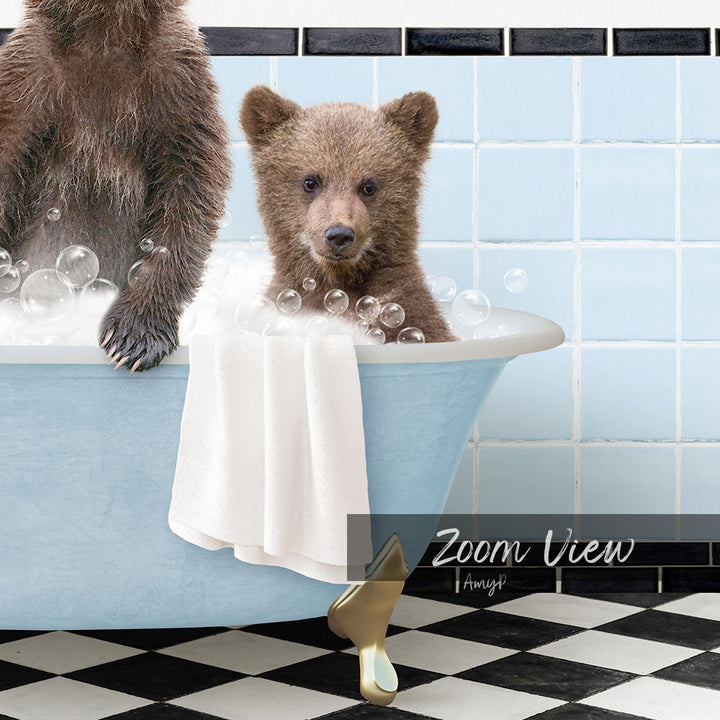A young bear cub sitting in a blue bathtub, surrounded by bubbles, with a towel draped over the side of the tub.