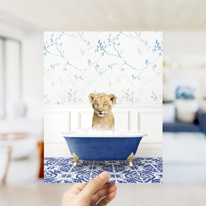 A young lion cub sitting in a blue bathtub filled with water, surrounded by a blue and white floral patterned wall.