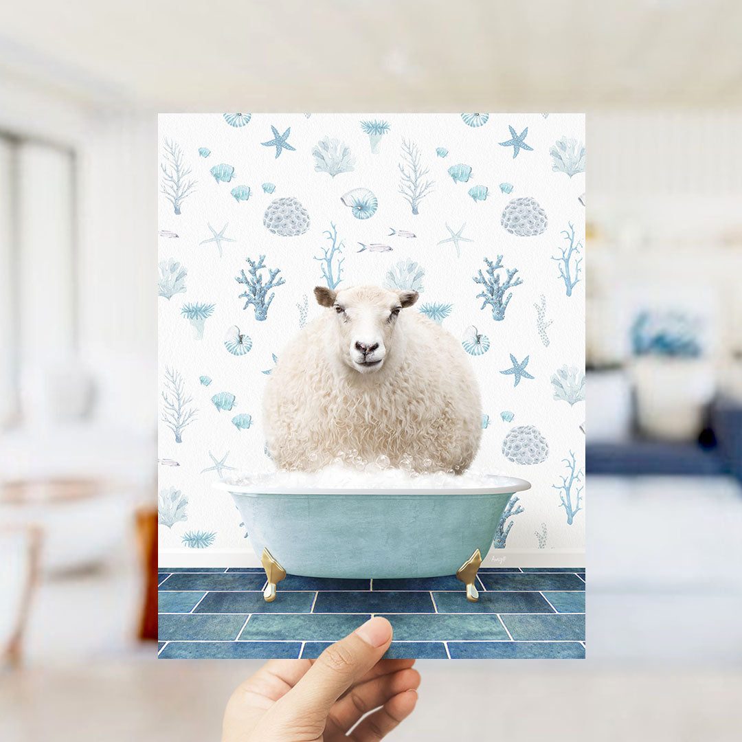 A hand is holding up a print featuring a sheep sitting in a bathtub filled with bubbles, surrounded by a pattern of blue and white marine life.