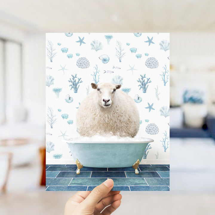 A hand is holding up a print featuring a sheep sitting in a bathtub filled with bubbles, surrounded by a pattern of blue and white marine life.