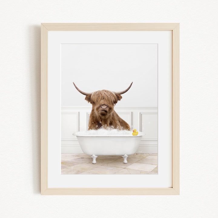A brown cow with long horns is sitting in a white bathtub filled with water, with a yellow rubber duck floating in the tub.