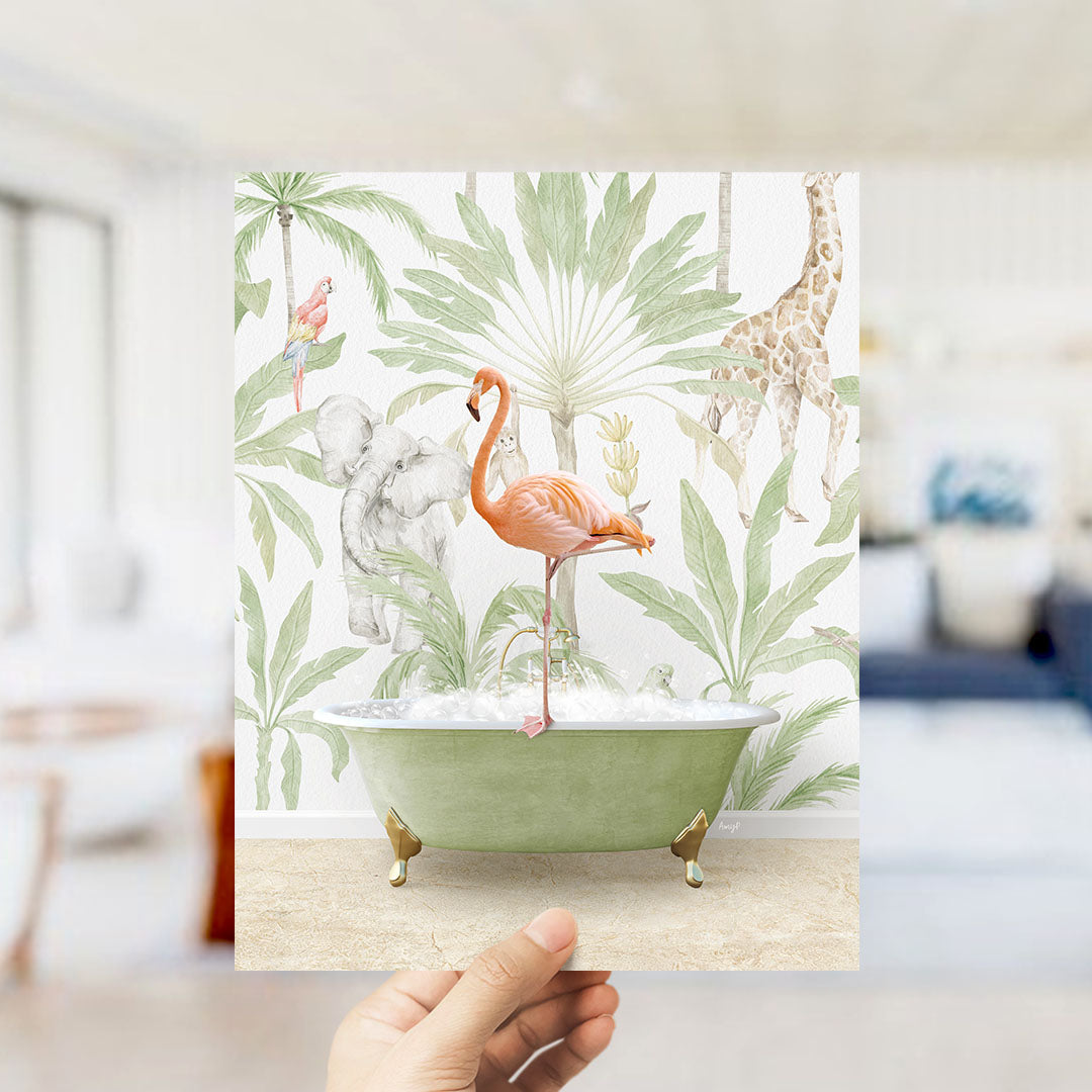 A hand holds up a framed print featuring a vibrant illustration of a flamingo sitting in a bathtub surrounded by tropical foliage, including a giraffe and an elephant.