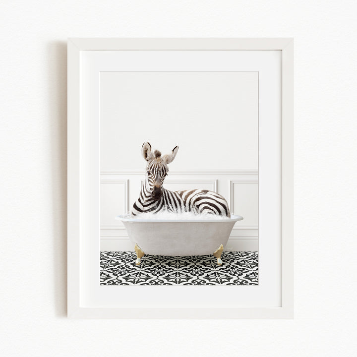 A zebra is sitting in a white bathtub, surrounded by a black and white patterned floor.