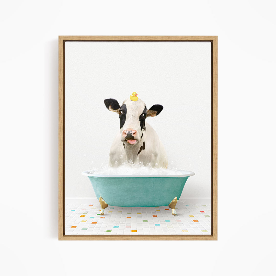 A black and white cow is sitting in a blue bathtub filled with bubbles, with a yellow rubber duck perched on its head.