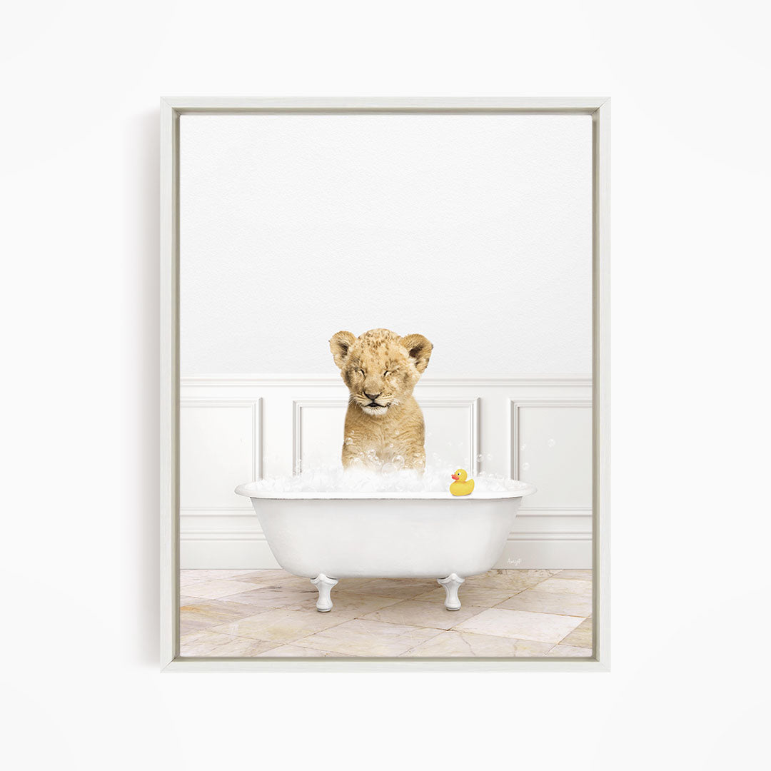 A young lion cub is sitting in a white bathtub filled with water, surrounded by a yellow rubber duck.