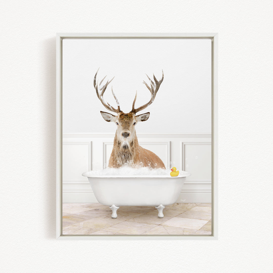 A deer with large antlers is sitting in a white bathtub filled with bubbles, with a yellow rubber duck floating in the water.