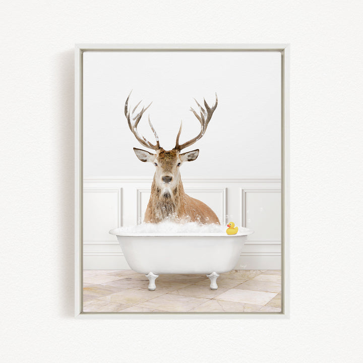 A deer with large antlers is sitting in a white bathtub filled with bubbles, with a yellow rubber duck floating in the water.