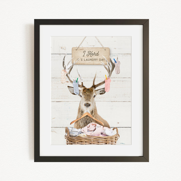 A framed image depicting a deer with antlers holding laundry, accompanied by a sign that reads "I herd it's laundry day".