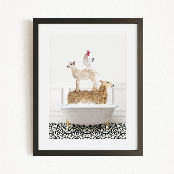 A framed image depicting a goat standing on a sheep's back while a rooster stands on top of the sheep, all in a white bathtub.